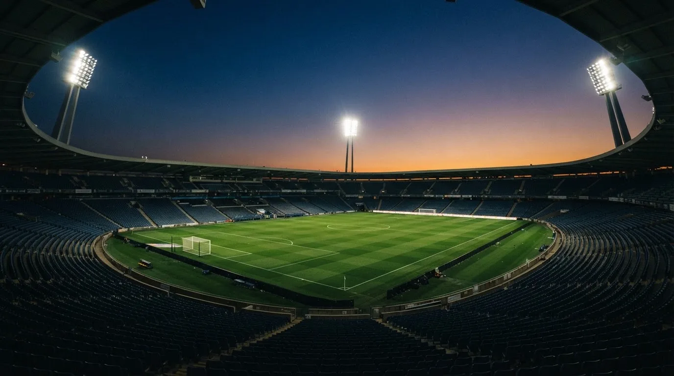 Een leeg voetbalstadion met lichtmasten bij schemering