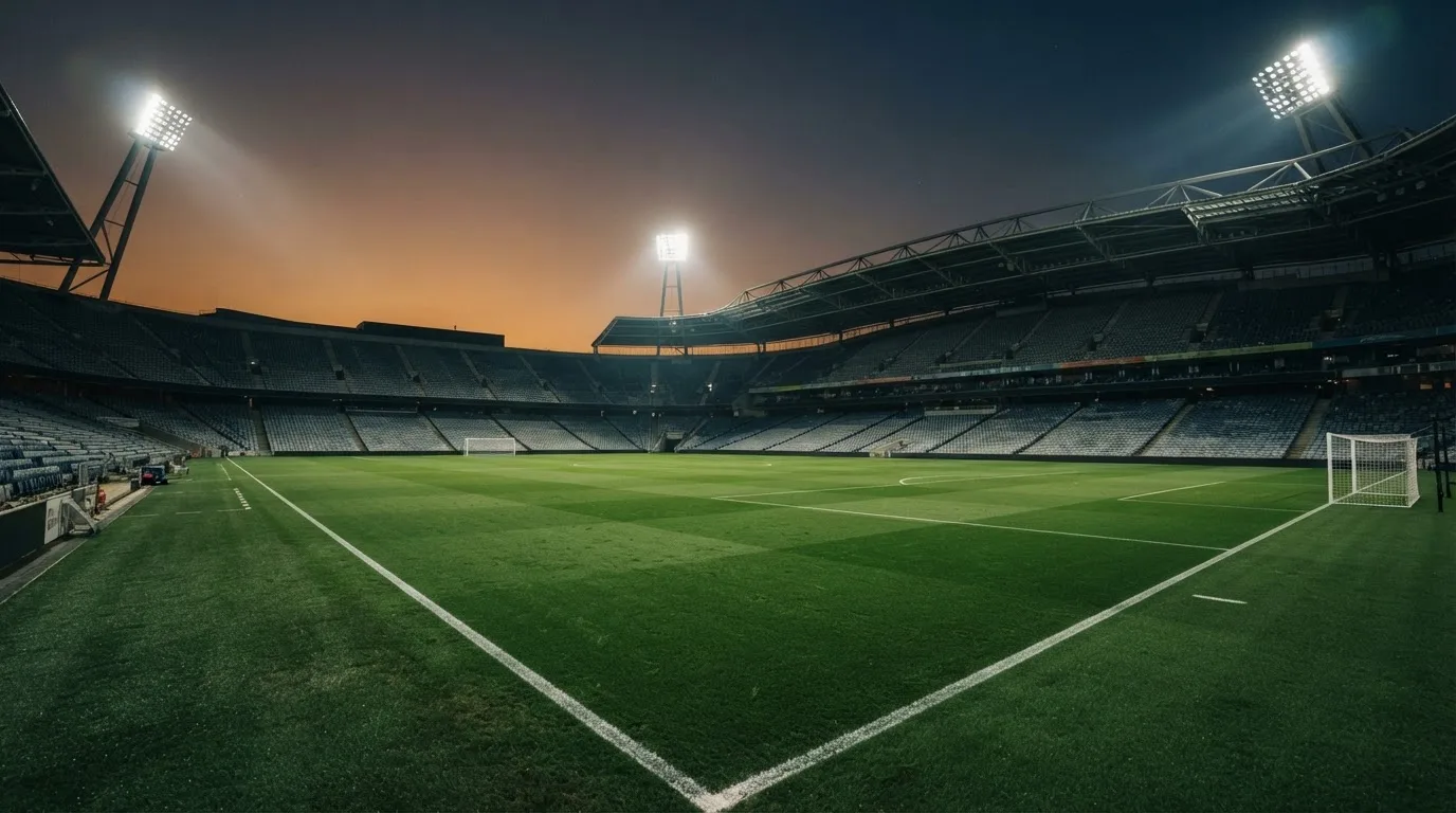 Een leeg voetbalstadion met lichtmasten bij schemering