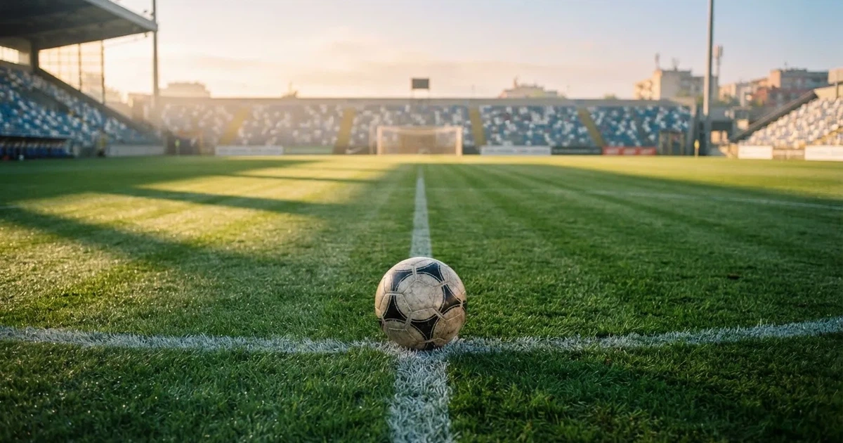 Een voetbal op de middenstip van een grasveld in het ochtendlicht